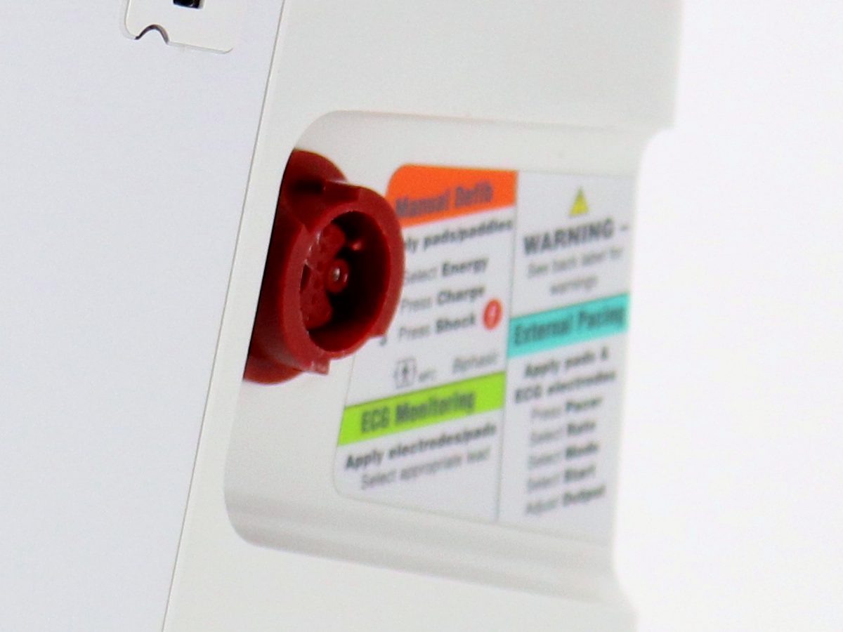 A close view of the red therapy cable connector on the side of the monitor, beside the printed instruction label applied next to it.