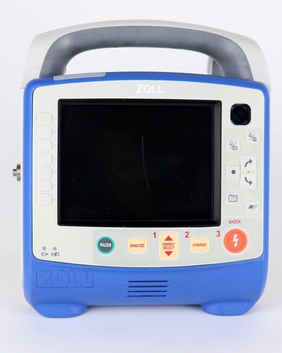 The same monitor/defibrillator photographed square from the front with its display off, showing its keypad, carry handle, and the wear on its case.