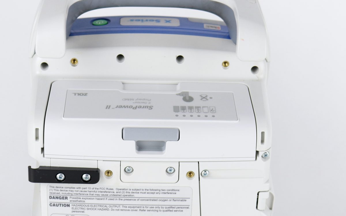 The back of the monitor, showing its battery bay, mounting fasteners, connector ports, and printed warning labels.